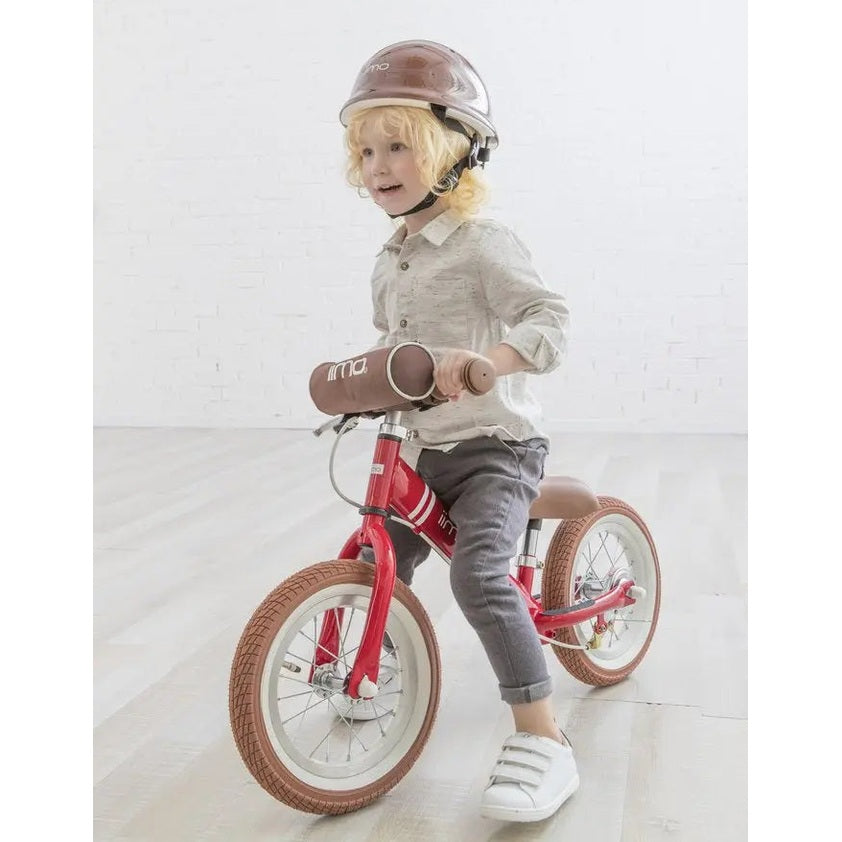 Iimo Balance Bike being ridden by a child in a beige shirt with brown helmet on a red frame with brown tires.