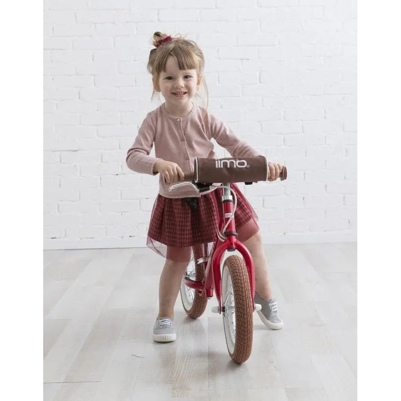 Iimo Balance Bike; pink frame with brown handlebar cover, toddler riding joyfully indoors.