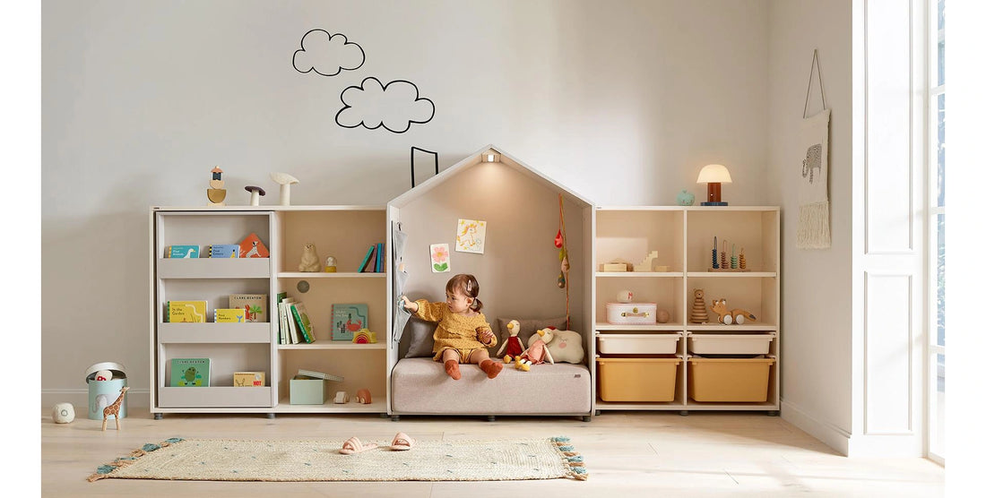 Child seated in the grey Eddi reading house reaching for a book in its side pocket; surrounding storage and props are separate.
