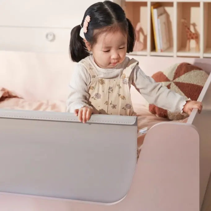 Iloom Eddi Kids Low Bed 1100W in light gray with pink accents; a toddler girl stands beside its low, rounded edge.