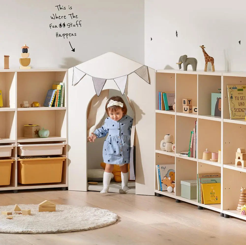 Iloom Eddi Kids Reading House Corner with Curtain: cozy beige wood shelves and a child entering the doorway.