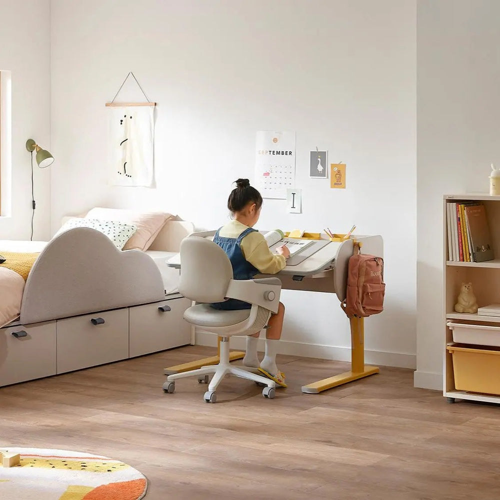 Iloom Jerome Motion Desk in light wood with yellow frame; child sits and studies at an adjustable sit-stand desk.
