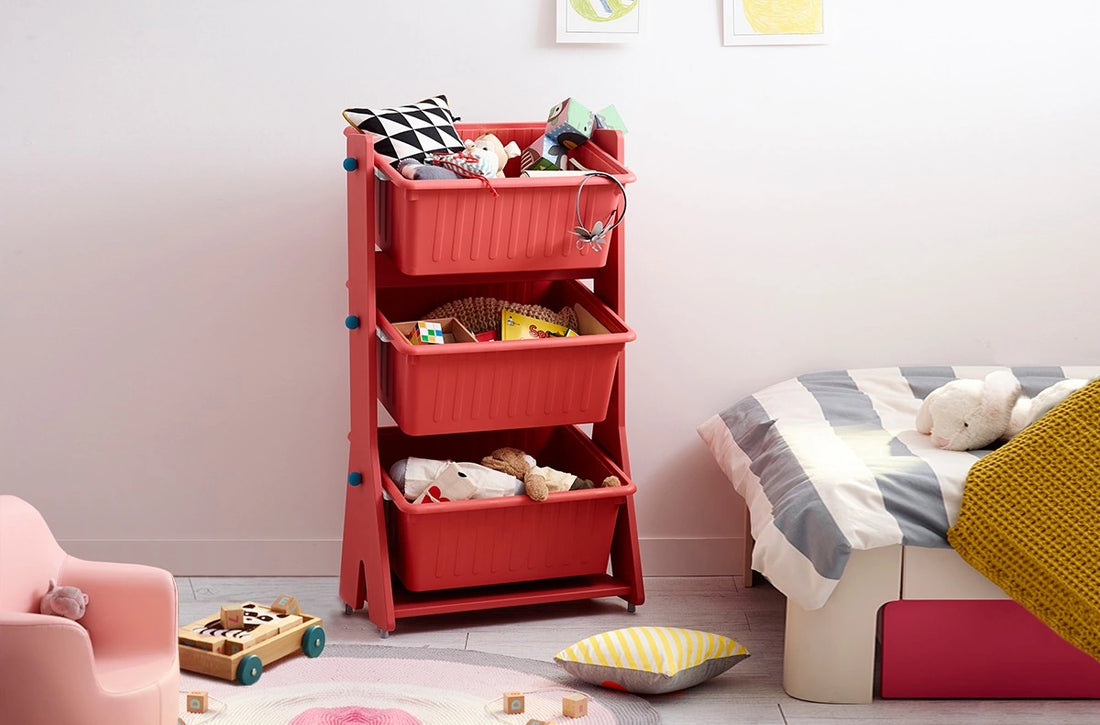 Sort playthings beside a bed: The curved-frame organizer is shown with three red bins and contrasting sky-blue side accents.