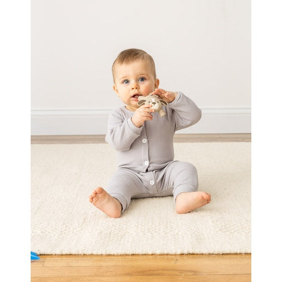 Itzy Ritzy baby molar teether held by a baby in a gray onesie on a rug, beige animal silicone teether