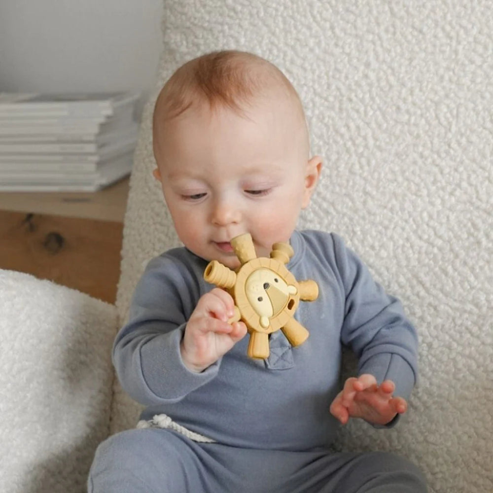 Itzy Ritzy wooden lion teether in natural wood, held by a baby in a blue outfit.