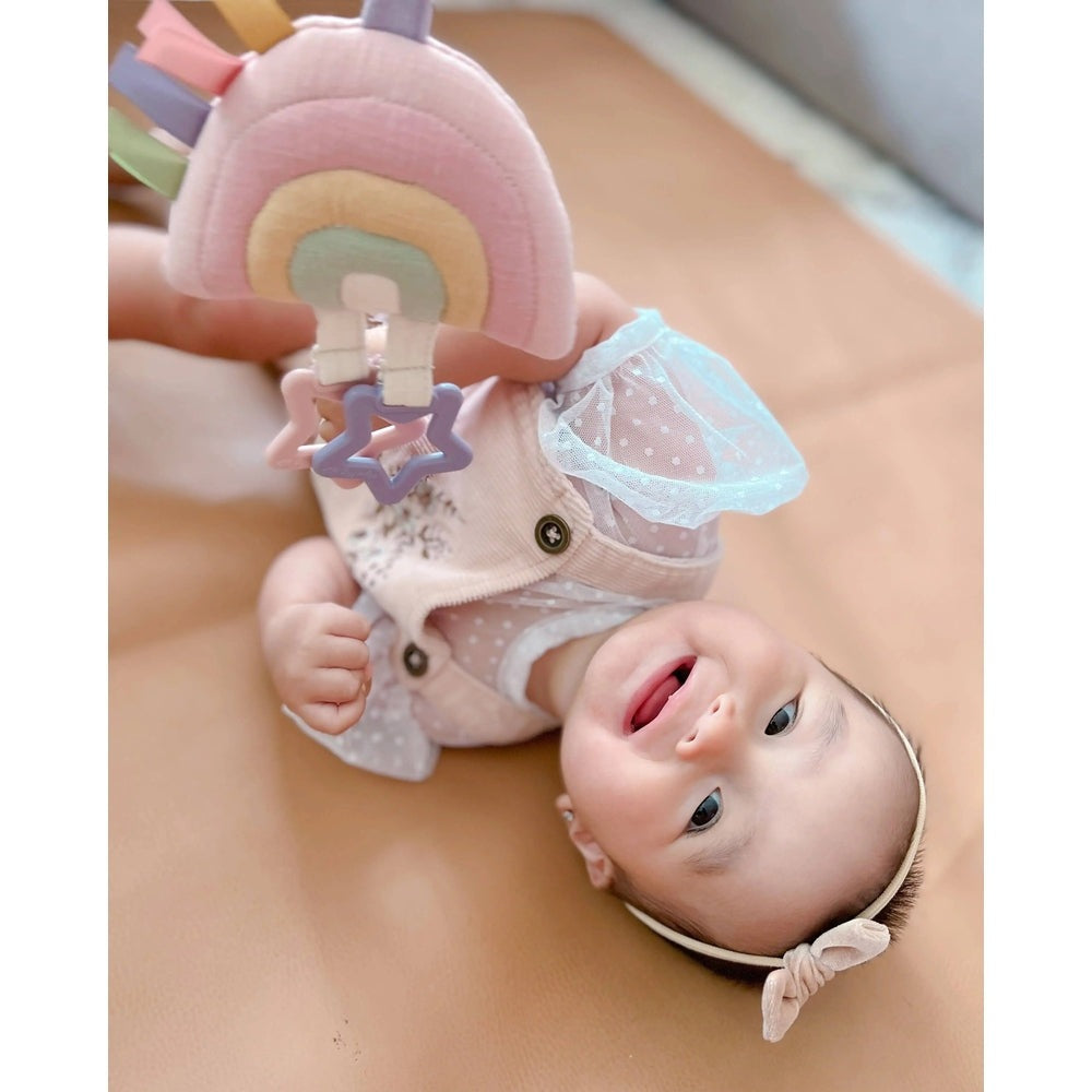Itzy Ritzy Bitzy Bespoke Ritzy Jingle Attachable Travel Toy, pastel rainbow plush with star clip attached to baby's outfit as they giggle.