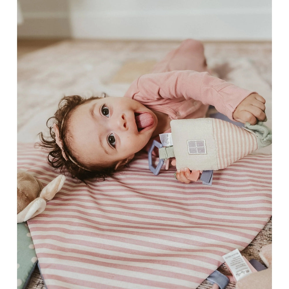 Itzy Ritzy Bitzy Bespoke Ritzy Jingle Attachable Travel Toy; soft pastel teething toy with ribbons grabbed by a curious baby.