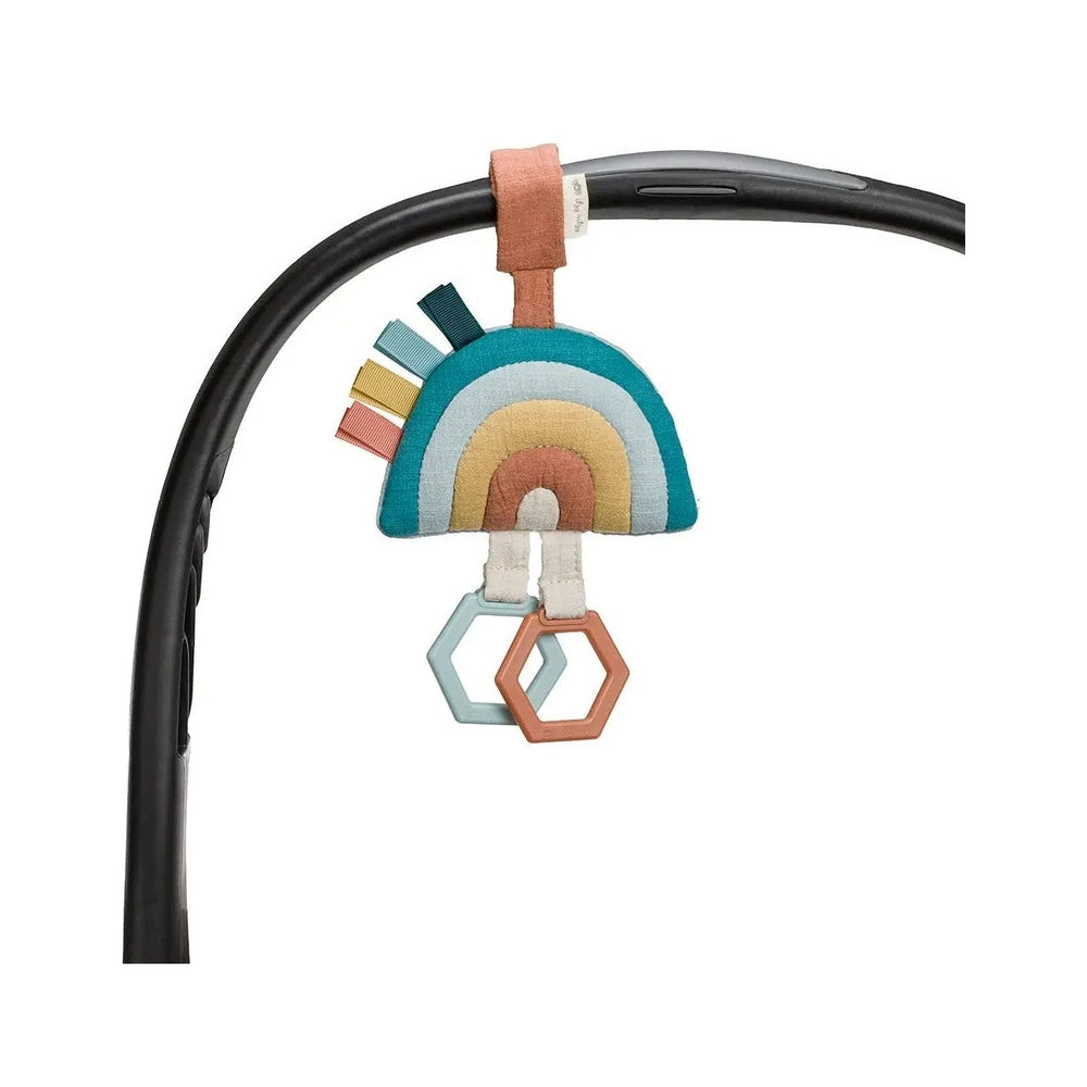 Itzy Ritzy Bitzy Bespoke Ritzy Jingle Attachable Travel Toy, rainbow plush teether with hex rings attached to a stroller bar