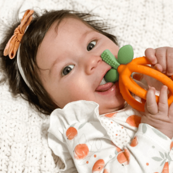 Itzy Ritzy Bitzy Biter Lemon Ball Teether, orange ring with green leaves being chewed by a baby.