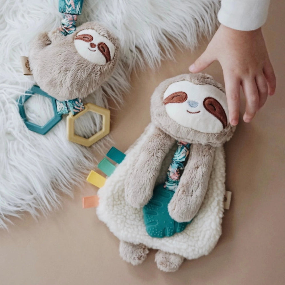 Itzy Ritzy Itzy Friends Link & Love Activity Plush: two beige sloth loveys with teal teether and colorful tabs; a child taps one.