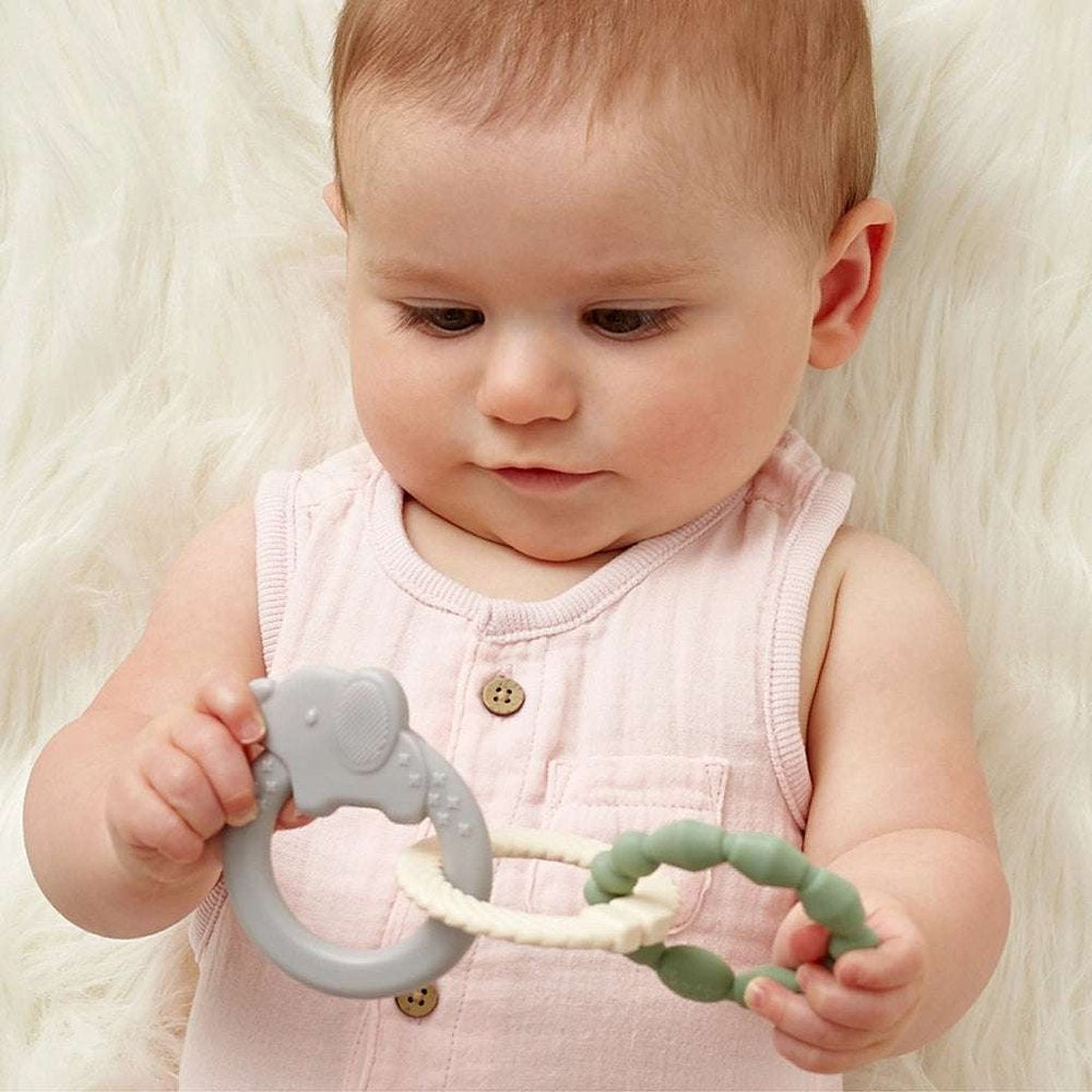 Itzy Ritzy Itzy Loops teething toy with gray ring and green beads, baby wearing pink sleeveless outfit.