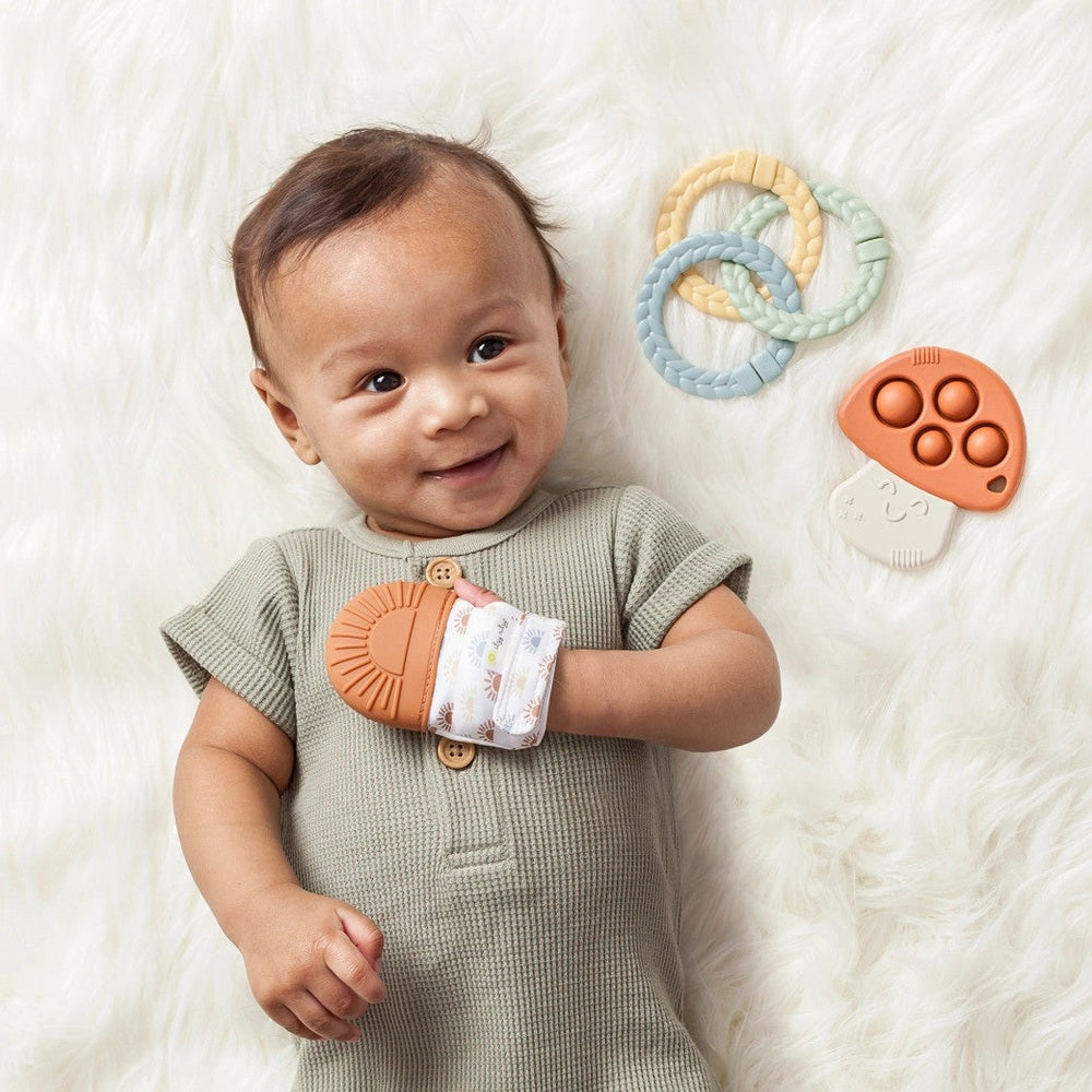 Itzy Ritzy teether gift set with 3 pastel silicone rings and an orange hand-teether beside a baby