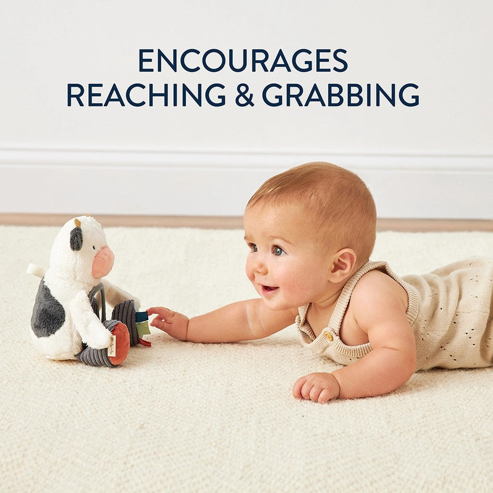 Itzy Ritzy Mirror baby toy with plush penguin and colorful blocks on a cream rug