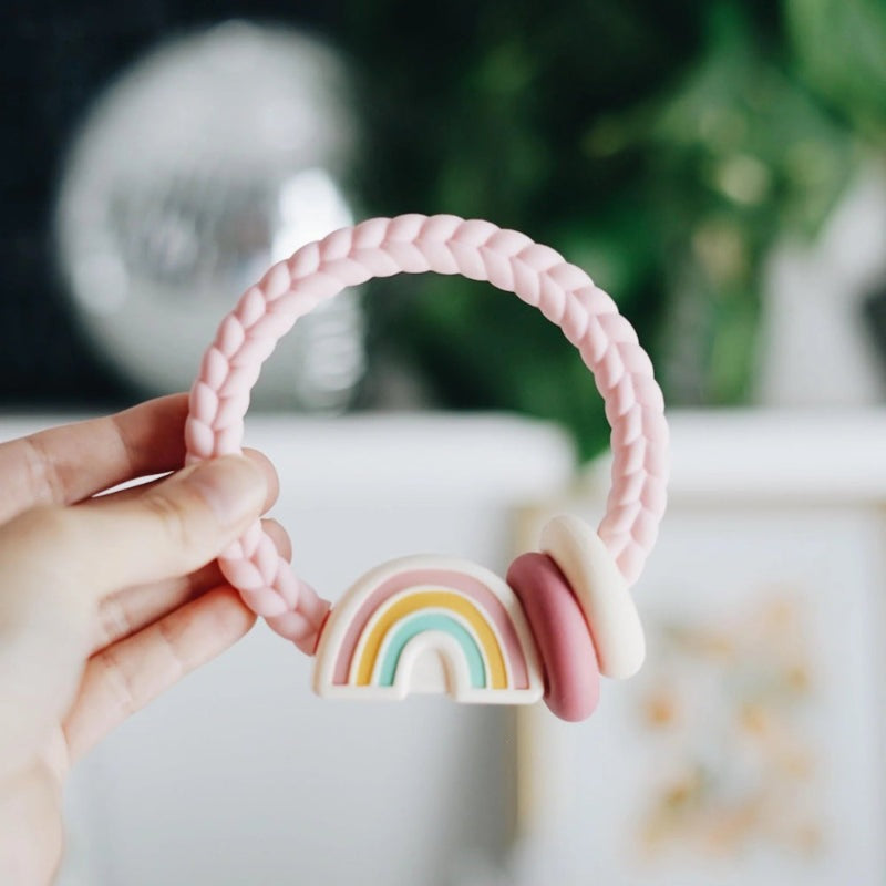 Itzy Ritzy silicone teether rattle in a pink braided ring with pastel rainbow charm