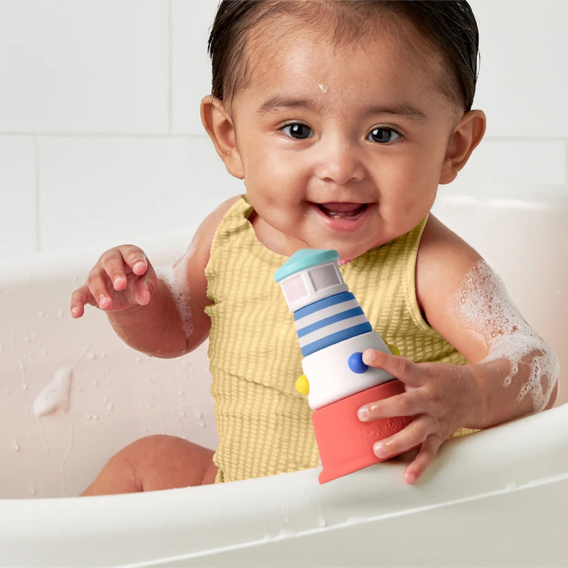 Itzy Ritzy Seaside Splash Gift Set bath toy: stackable lighthouse in blue, white, coral held by smiling baby.
