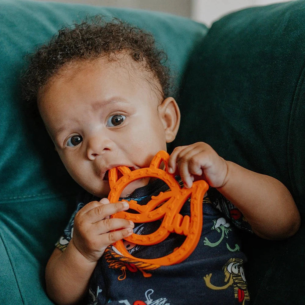 Itzy Ritzy silicone teether in bright orange; baby holds and chews the ring.