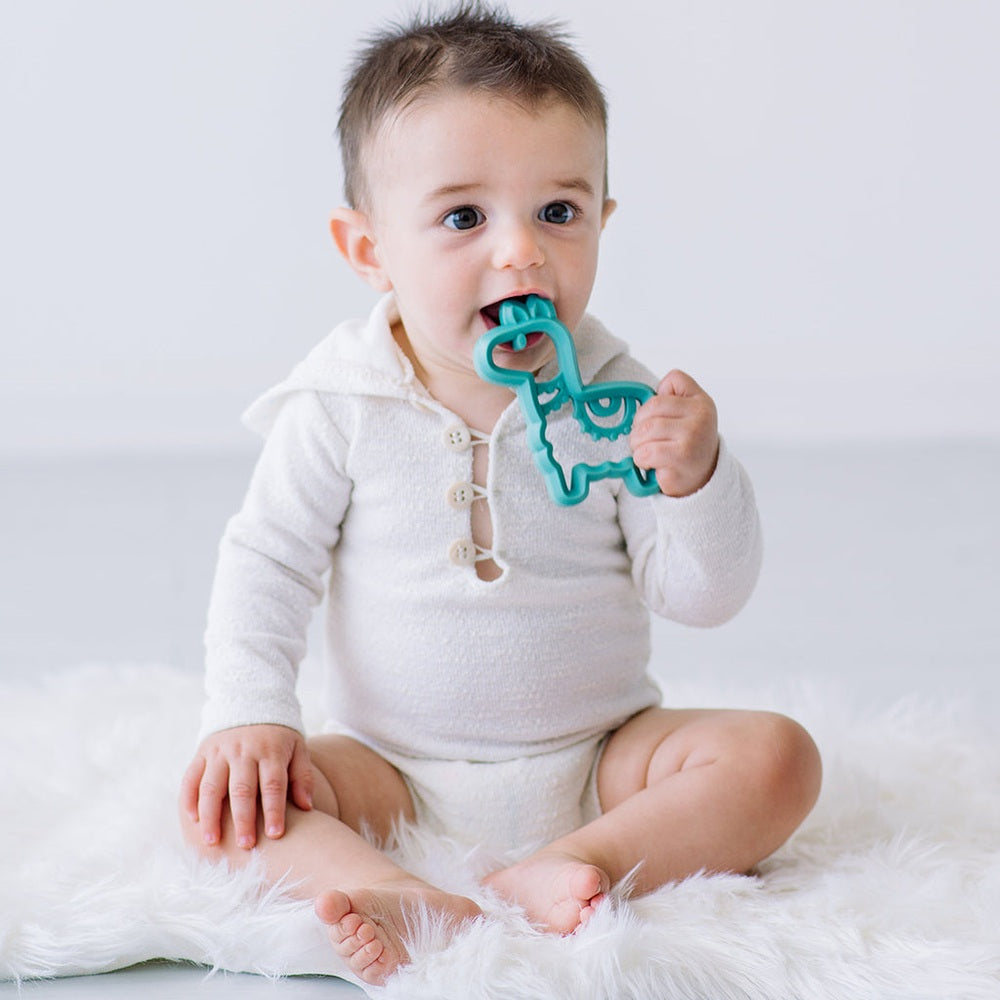 Itzy Ritzy silicone teether llama in teal held by baby during teething