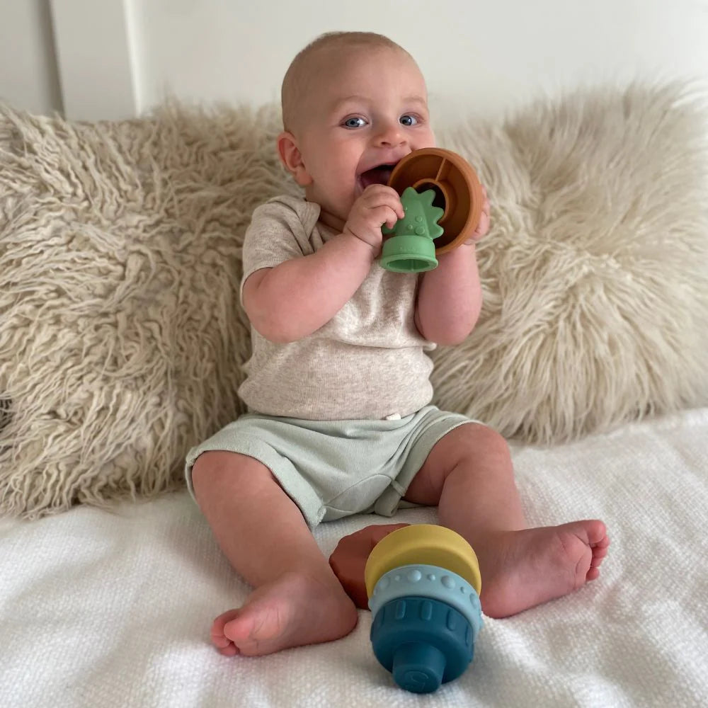 Itzy Ritzy silicone stacking toy set with two colorful rings; baby holds a green top piece.