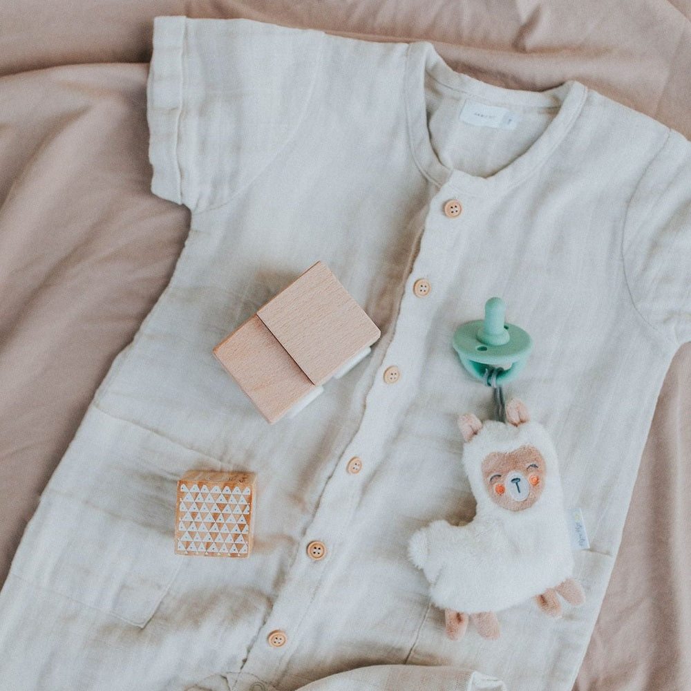 Itzy Ritzy Sweetie Pal pacifier and plush bear with mint clip on beige baby onesie