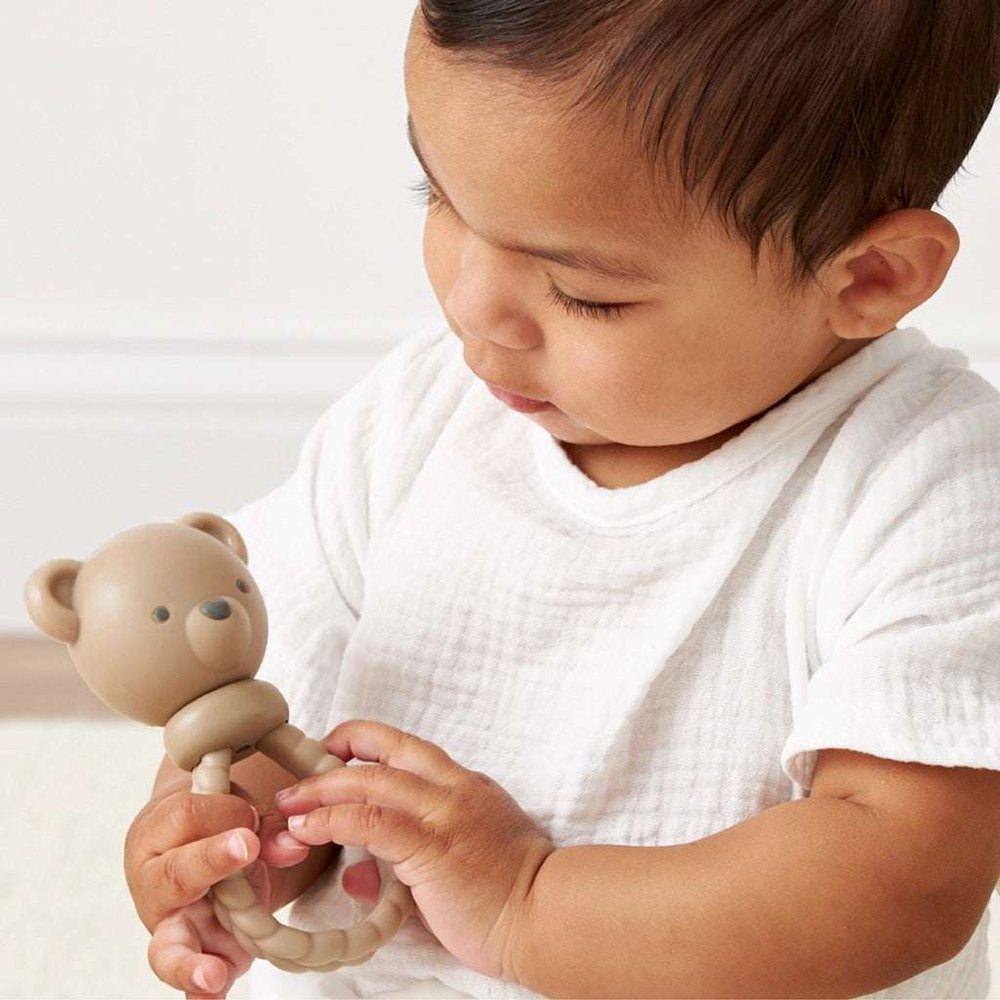 Itzy Ritzy Sweetie Rattle Bear teething toy in beige held by a baby