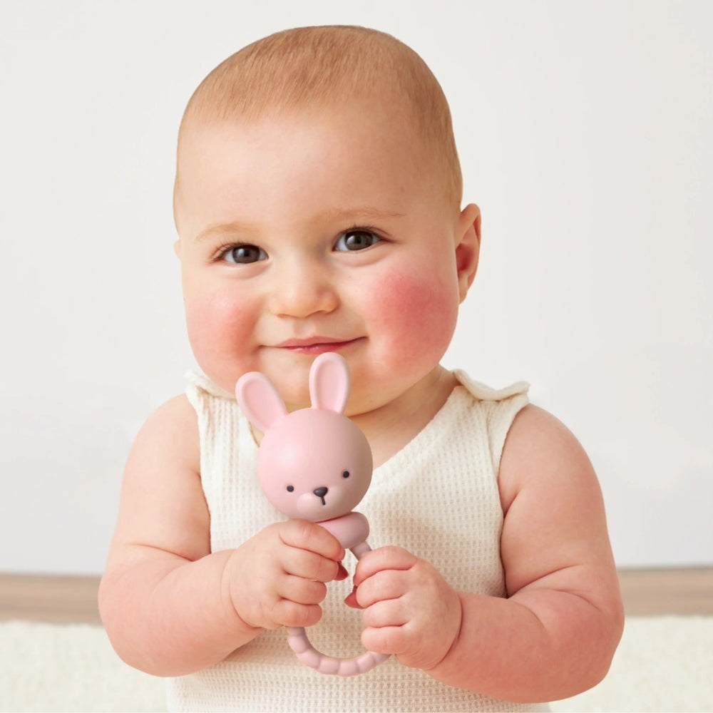 Itzy Ritzy Sweetie Rattle Pink Bunny held by a smiling baby, showcasing a soft pastel bunny rattle.