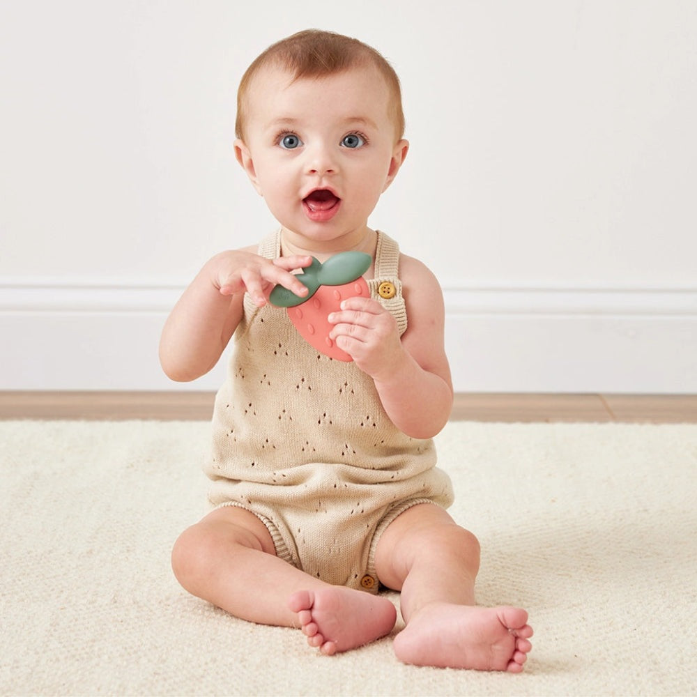 Itzy Ritzy Sweetie Shake Rattle & Teether strawberry teether with green leaves held by baby.