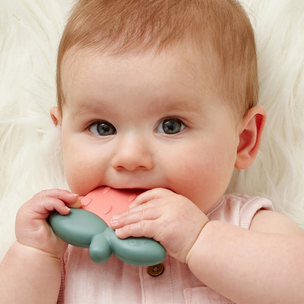 Itzy Ritzy Sweetie Shake Rattle & Teether teething toy in pink and teal, held by baby