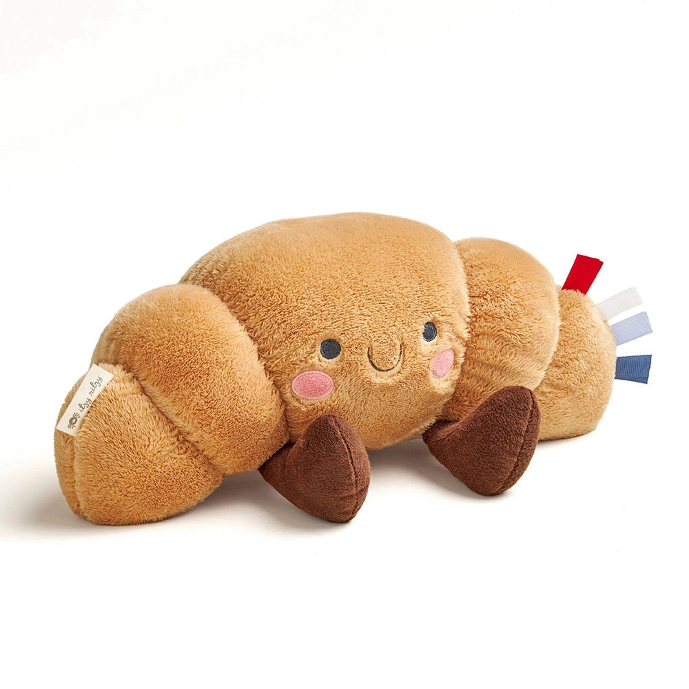 Itzy Ritzy Sweetie Snuggles Plush stuffed toy in tan with brown feet and pink cheeks, smiling beside rainbow ribbon tags