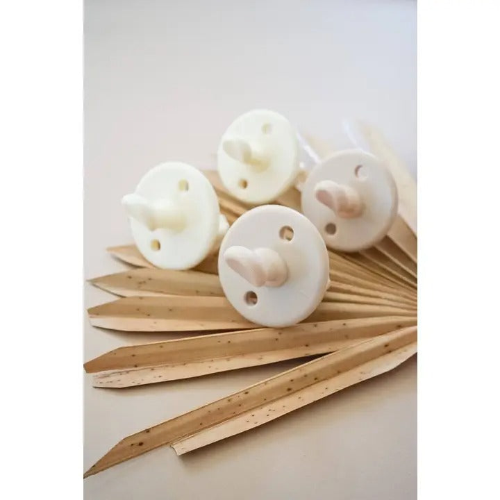 Itzy Ritzy Sweetie Soother Orthodontic Pacifier Sets (6-18M) in white, displayed on pale wooden decorative sticks.