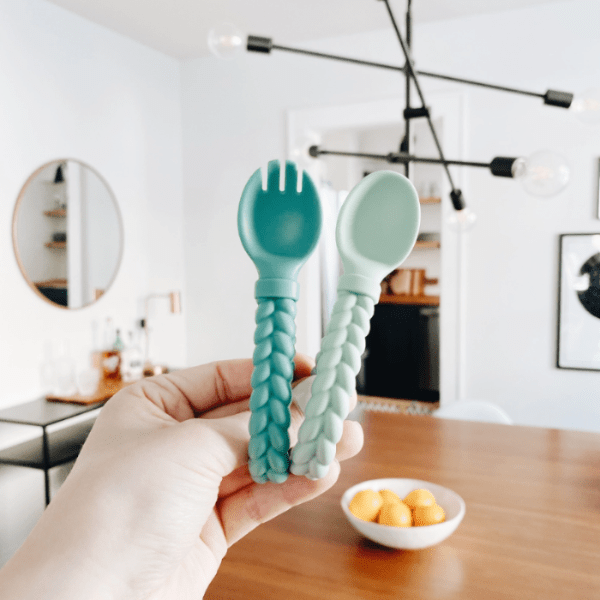 Itzy Ritzy Sweetie Spoon & Fork Set in teal and mint, braided handles held for mealtime.