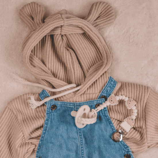 Itzy Ritzy Sweetie Strap Plus pacifier clip with white beads and bear charms on denim overalls