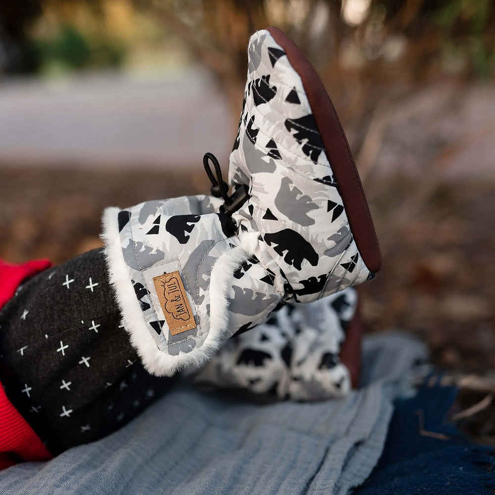 JAN & JUL Baby Stay-Put Bear winter booties in gray camo with white faux-fur trim and brown sole, on a baby's foot.