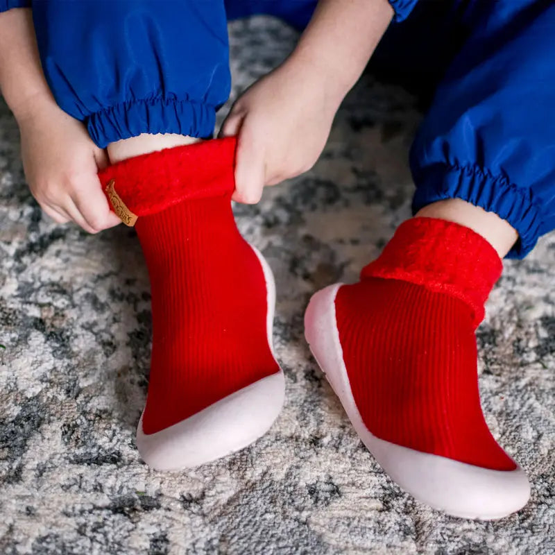 Jan & Jul Cozy Sock Shoes Red; red knit sock shoes with white soles, toddler feet being slipped on by a caregiver.