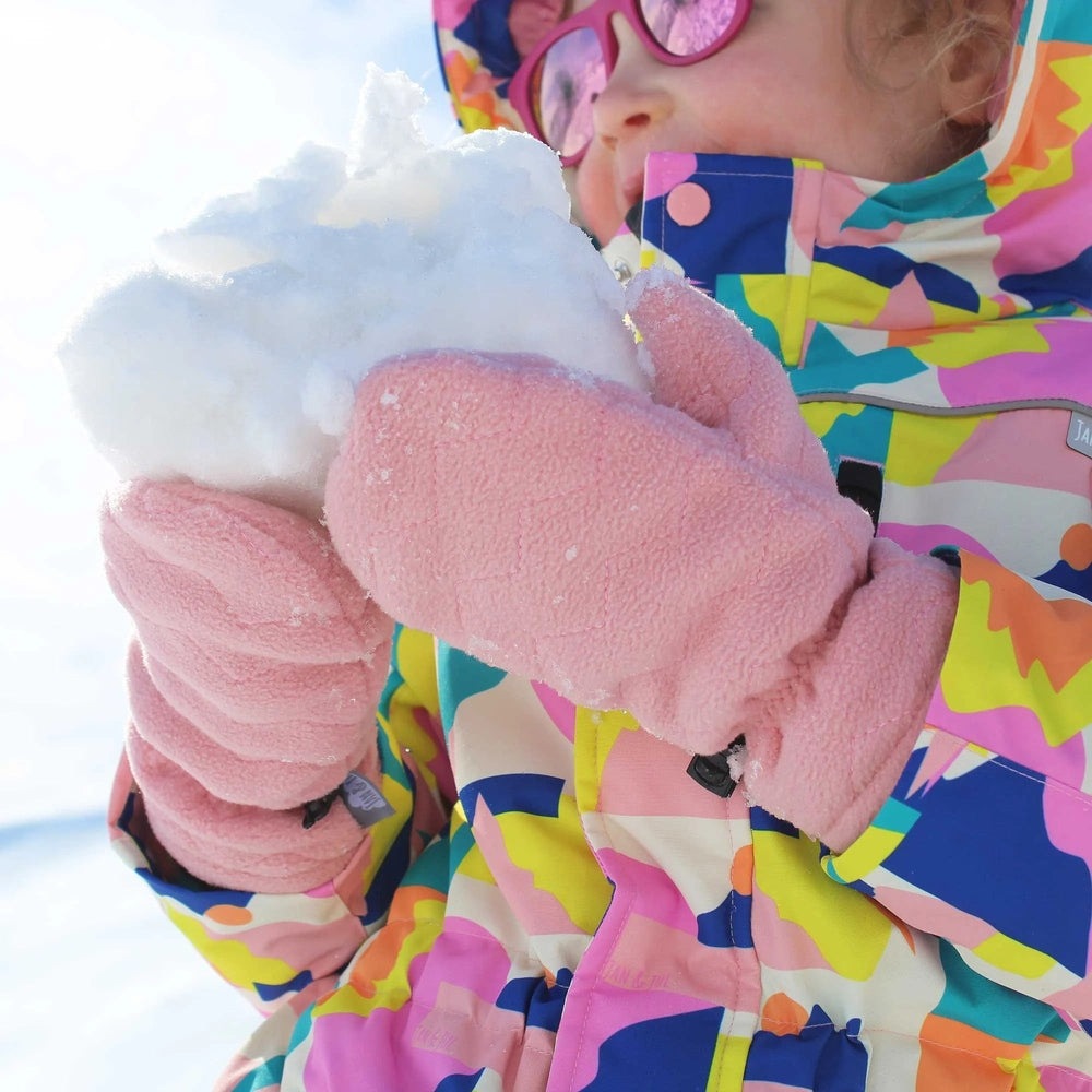 Jan & Jul Fleece Mittens Dusty Pink worn by a child in a bright jacket as they cradle a snowball.