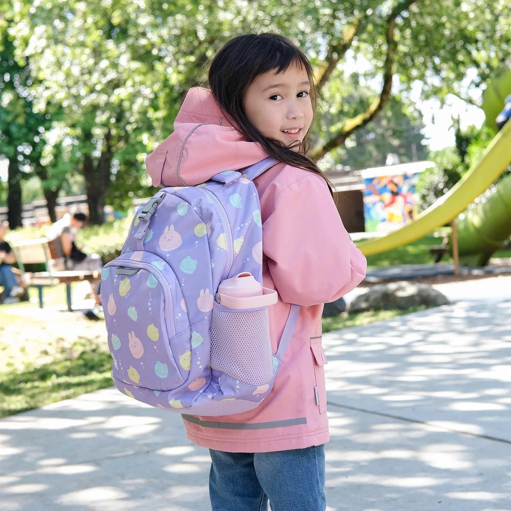 Jan & Jul Kids Backpack, lavender pastel animal print with mesh bottle holder, worn by girl in pink jacket at the park