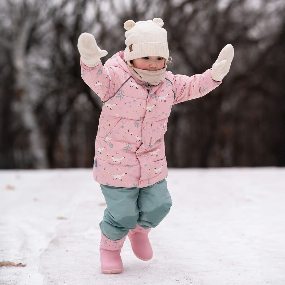 JAN & JUL bear knit hat in vanilla cream on a toddler wearing a pink winter snowsuit outdoors
