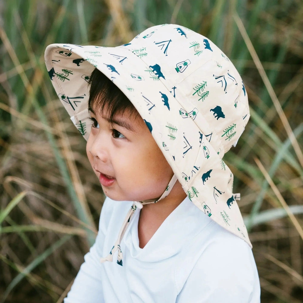 Jan & Jul Kids Cotton Adventure Hats Bear Camp beige hat with teal bears and pine print worn by a smiling toddler outdoors.