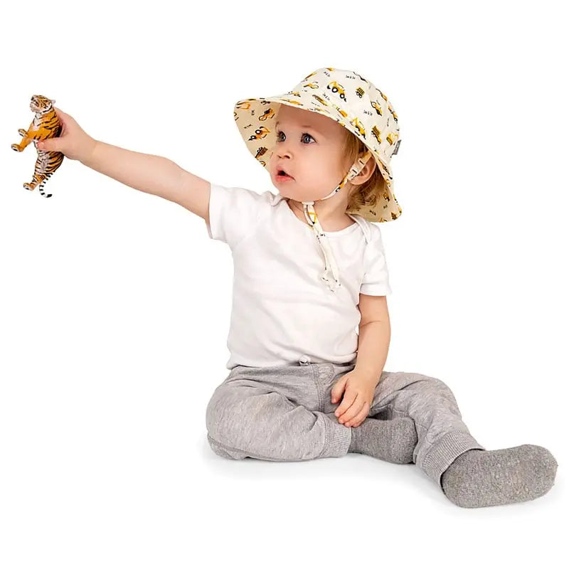 JAN & JUL Kids Cotton Bucket Hat Little Diggers beige hat with vehicle print, on toddler reaching with a tiger plush
