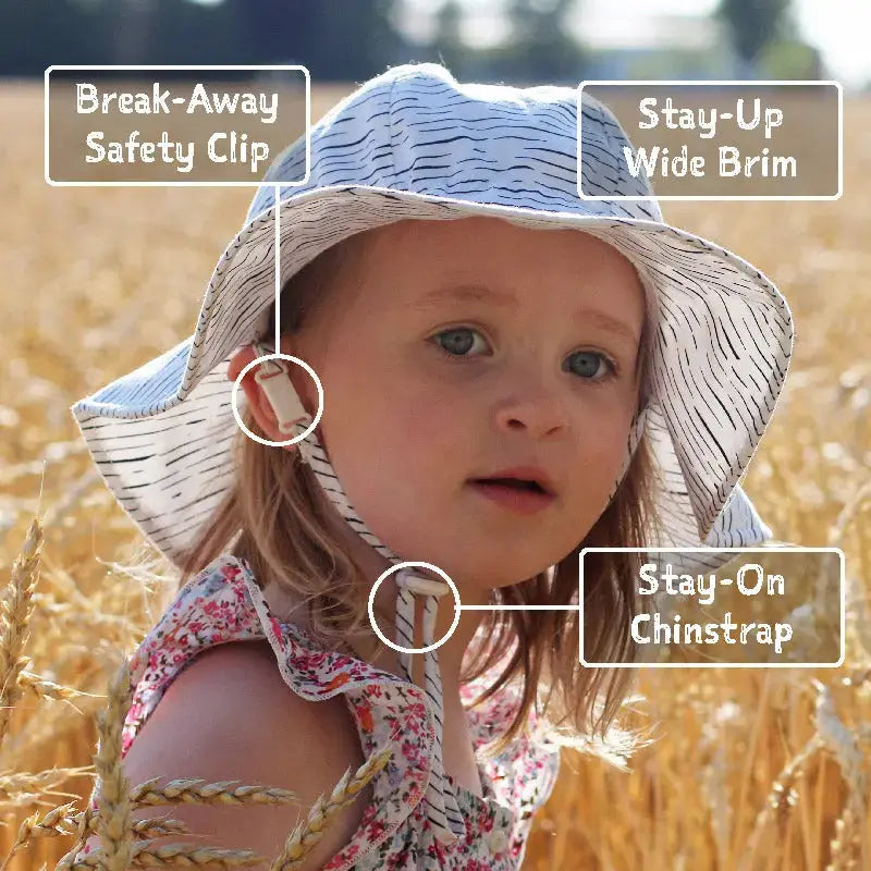 Jan & Jul Kids Cotton Floppy Hat Coral in a sunlit field; child wears the wide brim and secure chinstrap.