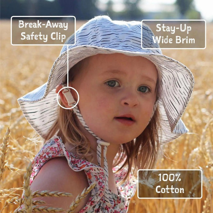 JAN & JUL Kids Cotton Floppy Hat Pink Prairie in a sunlit field, where a break-away safety clip secures the stay-up wide brim.