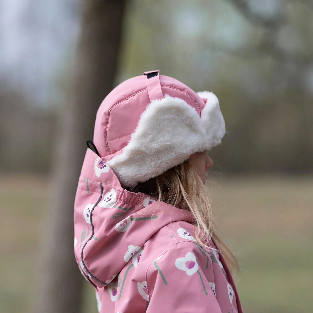 JAN & JUL Kids Insulated Winter Hats Dusty Pink worn by a child outdoors in a pink floral jacket with fluffy white lining.
