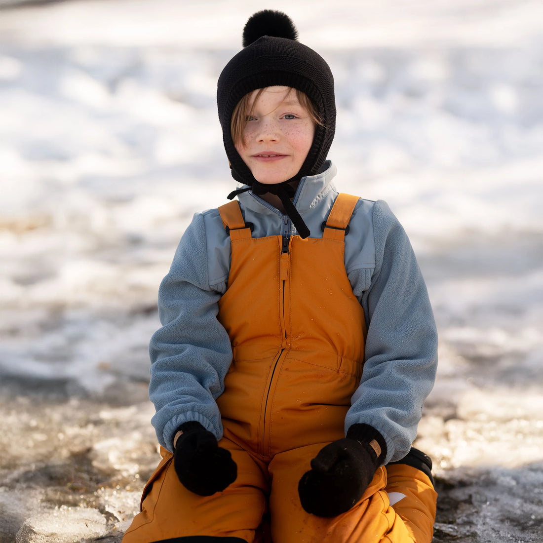 Child outdoors wearing the Jan & Jul Jet Black Pom-Pom Knit Hat.