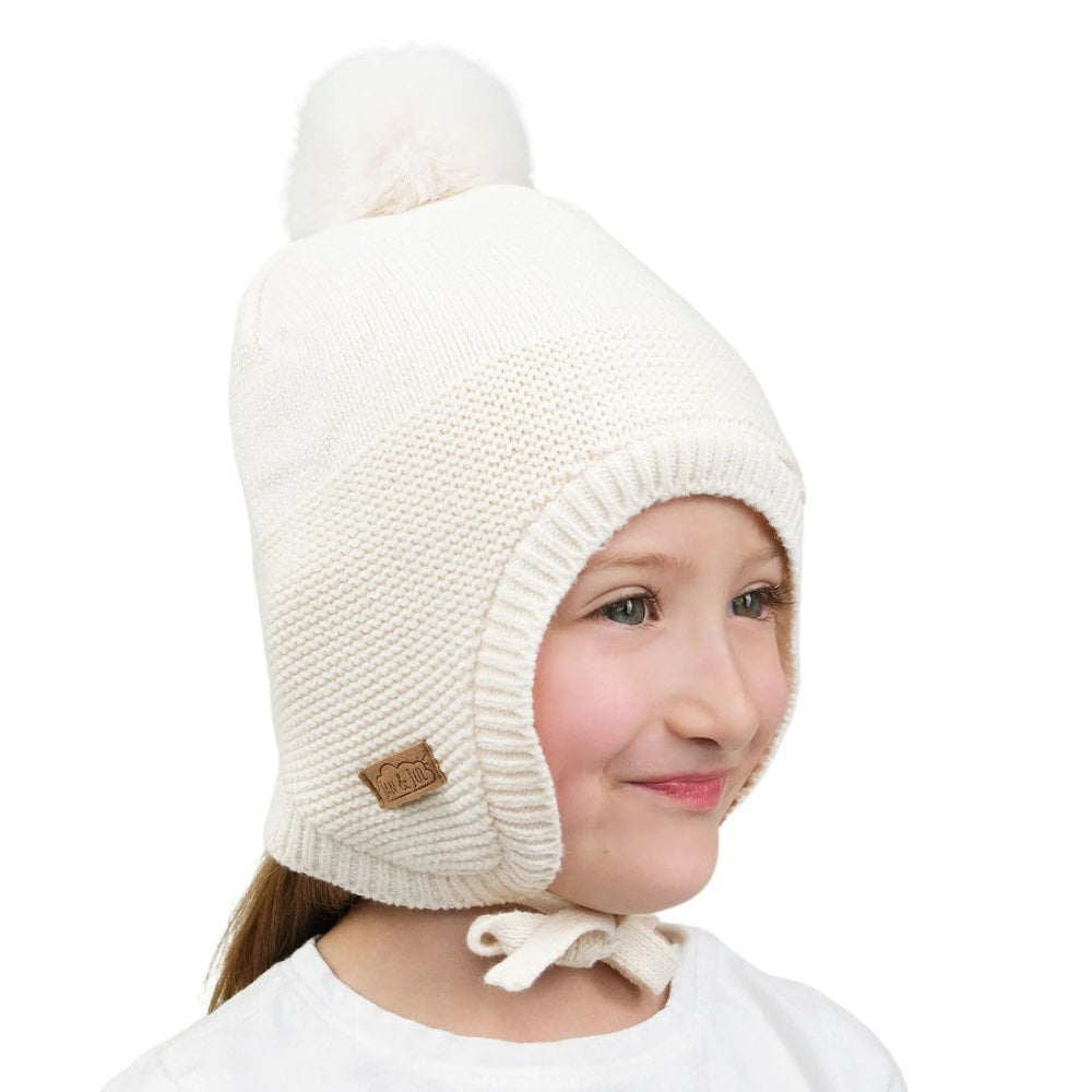JAN & JUL Kids Pom-Pom Knit Hat Vanilla Cream, cream knit with pom-pom, chin-tie under chin on a smiling child