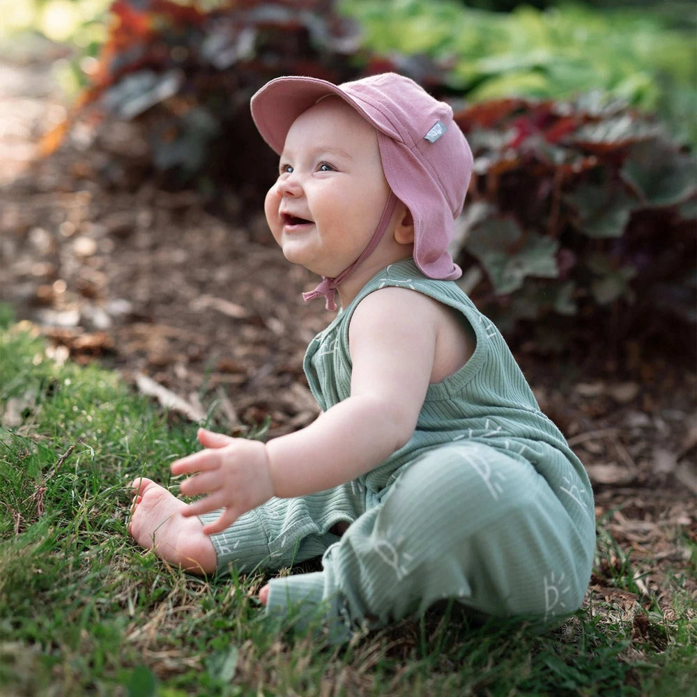 Jan & Jul Sun Soft Baby Cap dusty rose with chin strap on a smiling baby outdoors