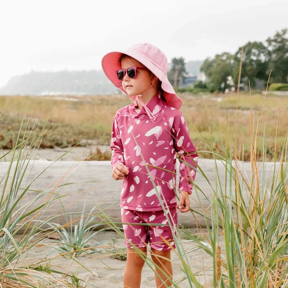 Jan & Jul Kids UV Rashguard Set Pink Petals with long sleeves and matching shorts, worn by a girl in a pink hat