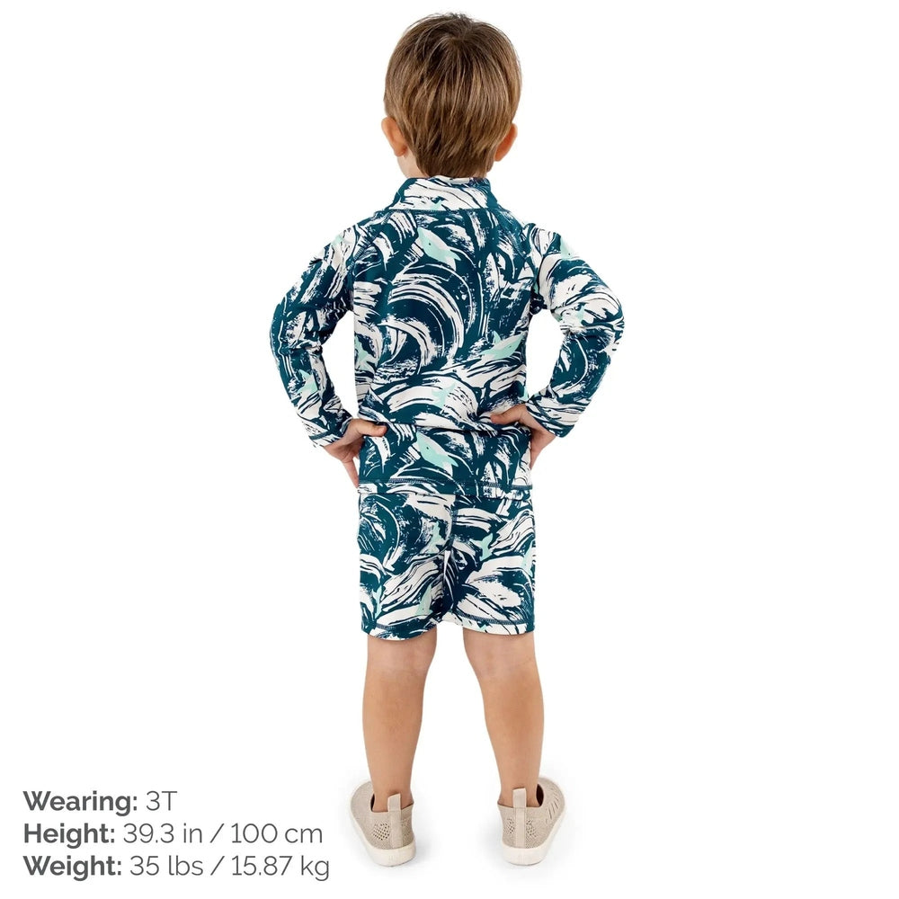 JAN & JUL Wave Rider kids UV rashguard set in teal and white waves, back view of child standing with hands on hips.