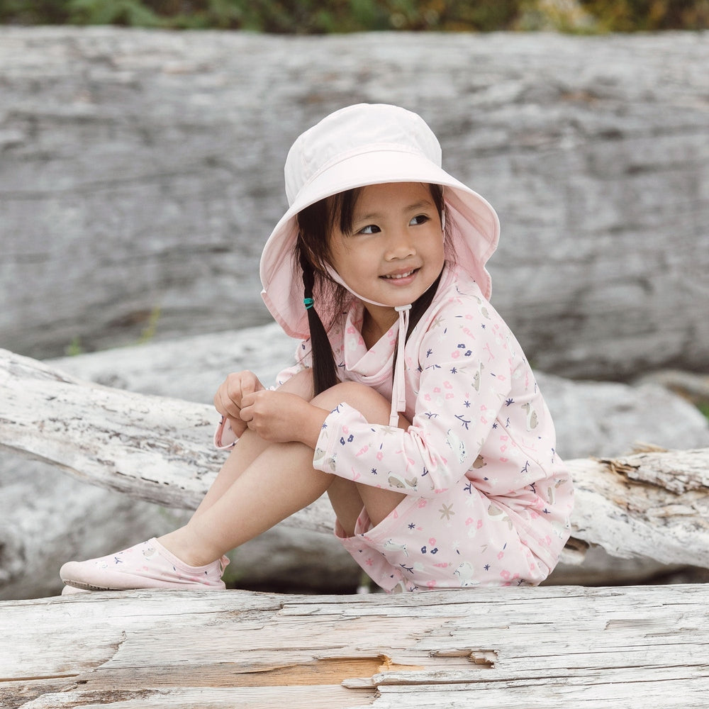 Toddler girl in a light pink sun hat and matching printed long-sleeve swim outfit
