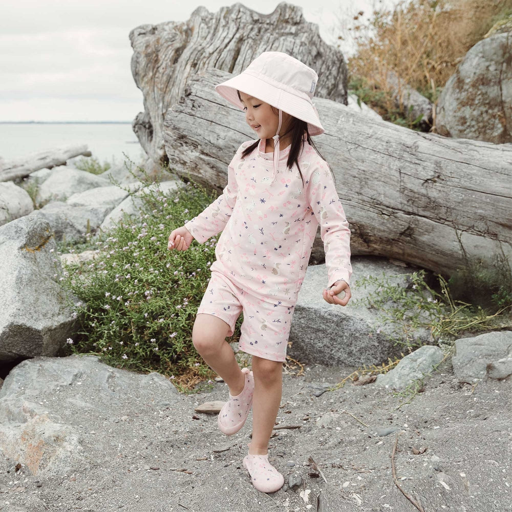 Child wearing a light pink printed sun-safe outfit with matching sun hat