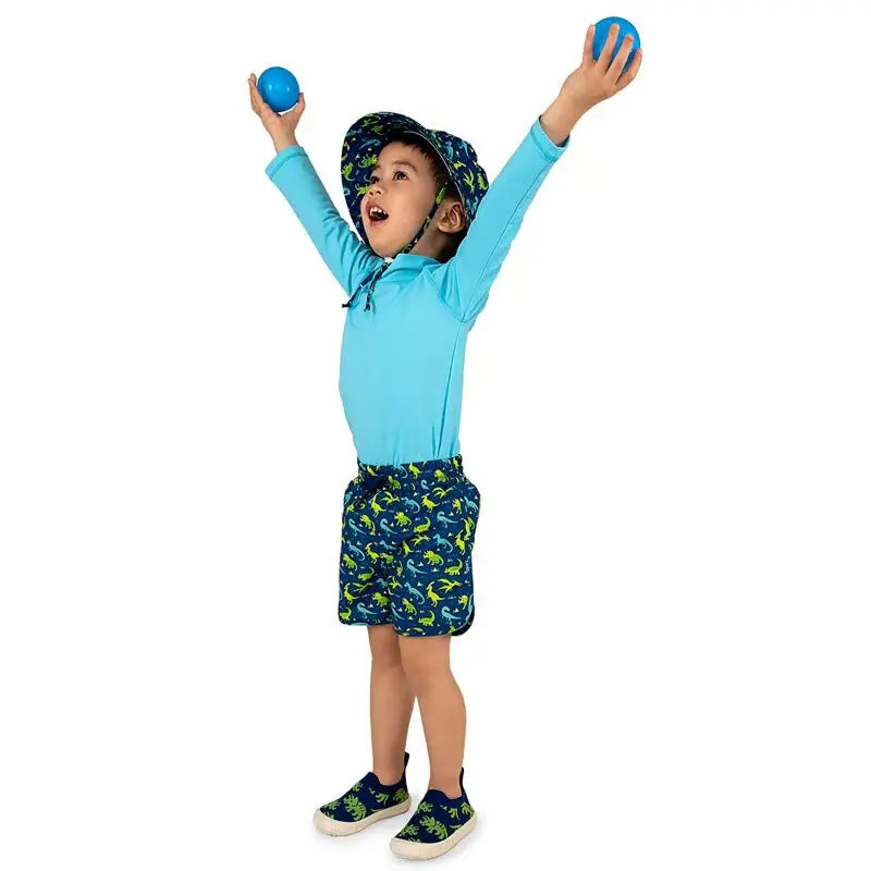 JAN & JUL Kids UV Rashguard Top Lagoon with matching dinosaur-print swim shorts; child cheers with arms raised.