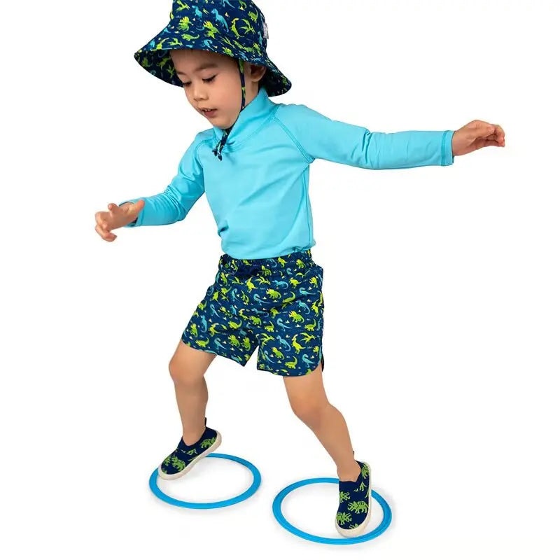 JAN & JUL Kids UV Rashguard Top Lagoon set, turquoise long-sleeve top with dinosaur-print swim shorts, child balancing on rings